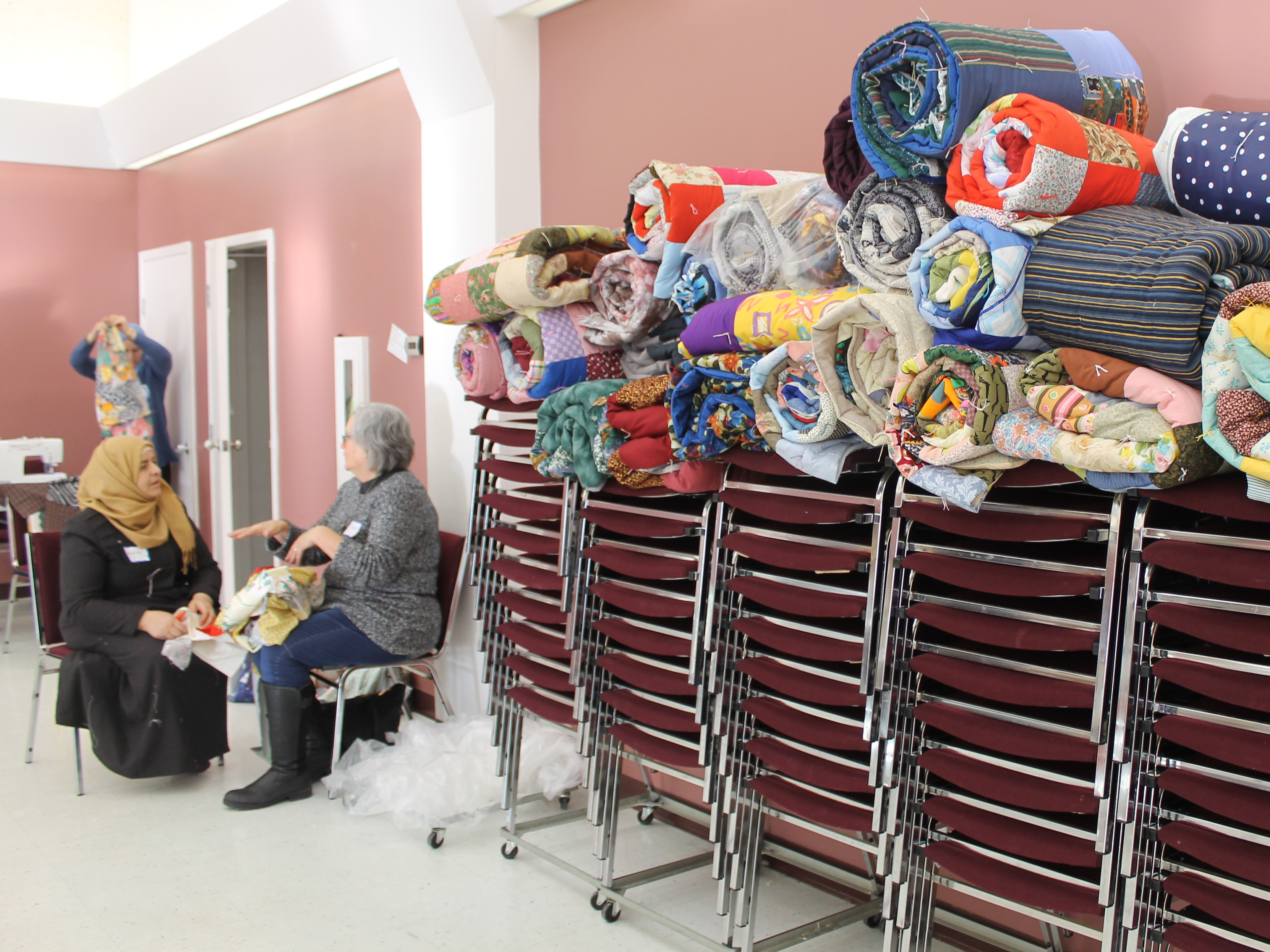 two women in conversation near a pile of MCC quilts